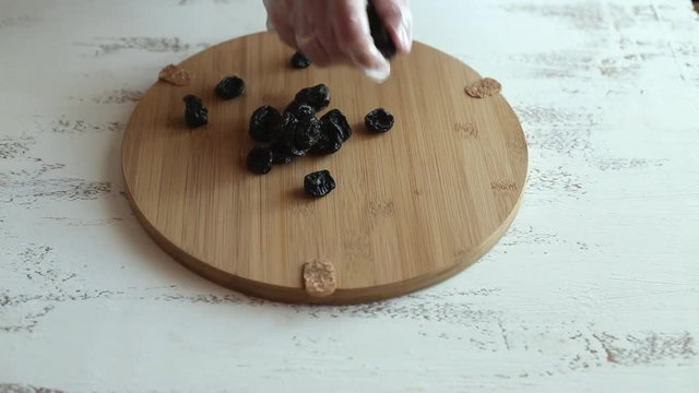 A young housewife pours prunes on a wooden table on a bright wooden table in the kitchen. Women's hands in white transparent culinary gloves. Vegan food. Close-up.