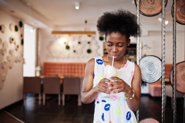 Сheerful african american young woman in summer dress at cafe drinking milkshake.