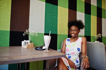 Сheerful african american young woman in summer dress at cafe with milkshake and dessert.