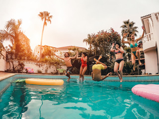 Group of happy friends jumping in pool at sunset time - Crazy young people having fun making party...