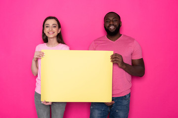Happy interracial couple holding empty yellow banner with copy space in studio