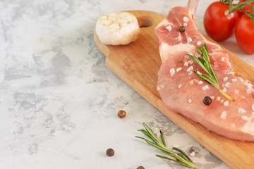 Preparing steak for cooking. On a wooden cutting board lies a raw piece of pork, tomatoes and garlic. Place for text, copy space.