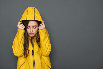 Waist up of sad Caucasian girl dressed in yellow raincoat in studio