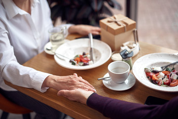 Close up male and female holding hands in cafe