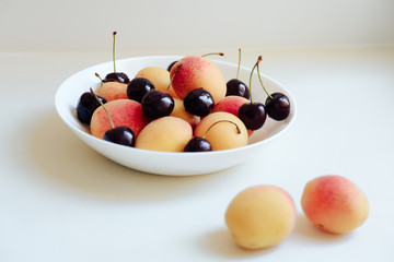apricots and cherry in a plate on a light background