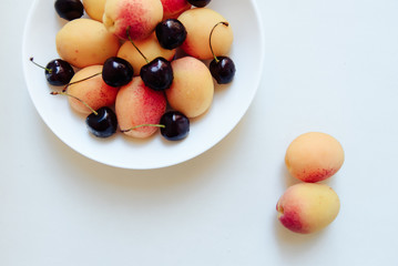 apricots and cherry in a plate on a light background