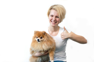happy girl shows thumb up on a white background, woman laughs with a small cute dog, pomeranian...