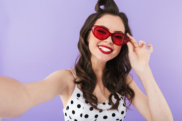 Naklejka premium Portrait of joyful pin-up woman 20s in retro sunglasses smiling while taking selfie photo