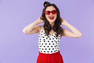 Portrait of content pin-up woman 20s in retro sunglasses smiling and posing at camera isolated over violet background