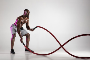 Young african-american bodybuilder training over grey background
