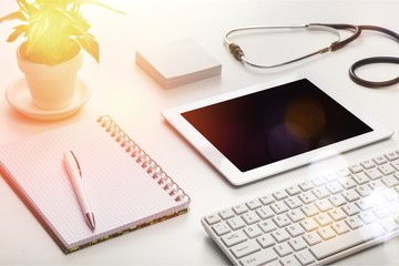 Digital tablet with green plant, pen, notebook and stethoscope on table in office