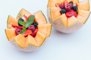 Food design and healthy nutrition concept. Delisious fresh raspberry, strawberry and blackberry with mint in carved melon. Cantaloupe with fruit against white background.