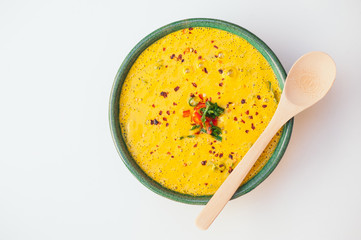 Hot creamy delicious soup with greenery and vegetables, wooden spoon on bowl, isolated over white...