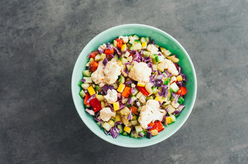 Top view of fresh vegetable salad with cauliflower, purple cabbage, chopped red bell pepper and cucumber. Delicious meal in bowl. Eating and nutrition concept