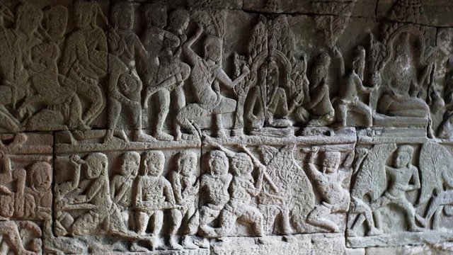 Close sliding view of detailed bas-reliefs on the stone wall in Bayon temple. Built in 12-13th century it stands at the centre of Jayavarman's capital, Angkor Thom. Cambodia