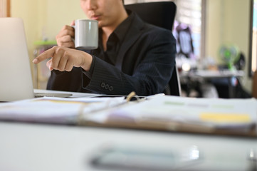 Cropped shot businessman using laptop and holding coffee mug on workplace.