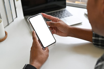 Cropped shot hands using mockup smartphone on office desk with clipping path.