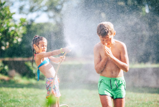 Two childs playing in garden, pours each other from the hose, makes a rain. Happy childhood concept image.