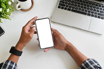 Cropped shot hands using mockup smartphone on office desk with clipping path.