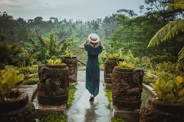 A young woman in a long dress and wearing a hat is standing with her back against the background of...