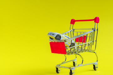 Toy car in small shopping cart on yellow background. Car rent and consumering concept with copy space.