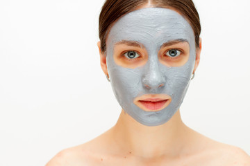 Portrait of young lady is looking at camera with joy while touching her face with clay mask while using procedures. white background. Beauty concept 