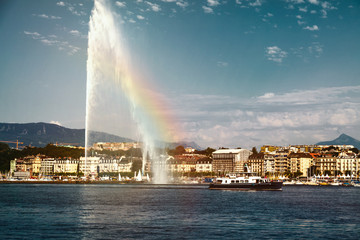 Naklejka na ściany i meble Beautiful sunset of the water jet fountain with rainbow in the lake of Geneva and the cityscape of Geneva, Switzerland