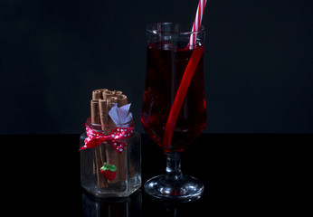 Red drink in glass and cinnamon sticks on black background.