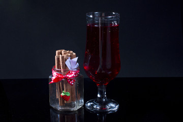 Red drink in glass and cinnamon sticks on black background.