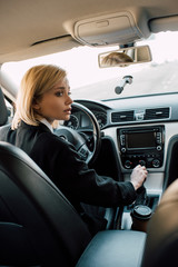worried blonde young woman holding gear shift handle while sitting in car