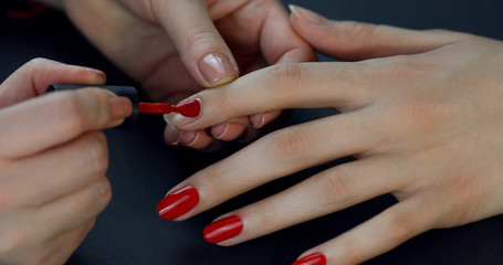 the manicurist paints the client's nails with red nail polish on a black background  Painting nails.
