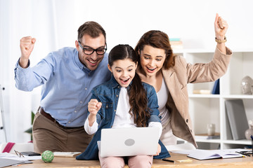 happy family celebrating triumph near laptop in office