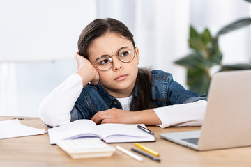 sad cute kid in glasses near laptop in office