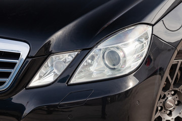 Obraz na płótnie Canvas Black car front double headlight view with dark gray interior in excellent condition in a parking space among other cars