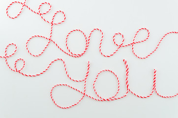 Love you words written with woolen red and white thread lettering, concept and isolated white background for Valentine's Day, copy space.