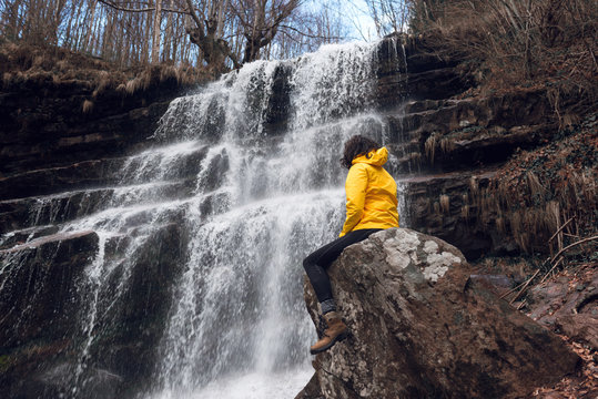 Woman Sitting By Waterfall	In Yellow Jacket