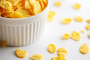 White cup with golden corn flakes, isolated on white background. Hopya crumbled around the cup. View from above