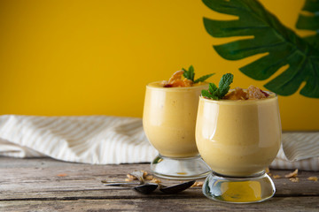 Two glasses of mango or pineapple milkshake or smoothie in a glass on the old wooden background. Summer refreshing drink concept.
