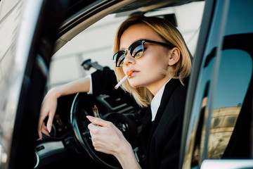 Fototapeta na wymiar blonde woman holding lighter with fire while smoking cigarette in car