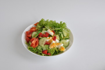 a mixture of hard cheese, cucumber, egg, lettuce, pepper on a white plate and a light background