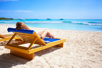 Holiday vacation beach - beautiful young girl relaxing on lounger on paradise caribbean beach with white sand and palms near blue sea on warm summer day