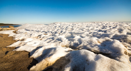 Fototapeta na wymiar Snow pile, hill. Large snow drift isolated on a blue sky background, outdoor view of ice blocks at frozen finland lake in winter