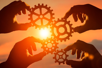 four gears in the hands of people against the sunset, the evening sky. interaction, movement, teamwork.