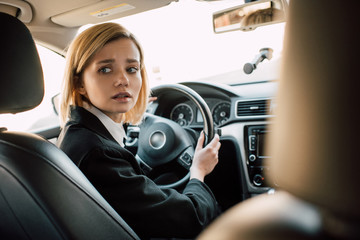 worried blonde woman holding steering wheel while sitting in car