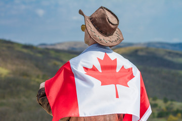 A man in a cowboy hat take canadian flag. A man in a cowboy hat and a leather jacket in the mountains take canadian flag