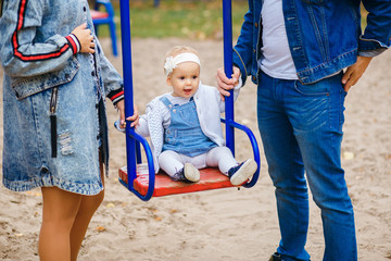 Fototapeta na wymiar Beautiful young parents, walk with a child, swing him on a swing, have fun and enjoy each other, happy family for a walk