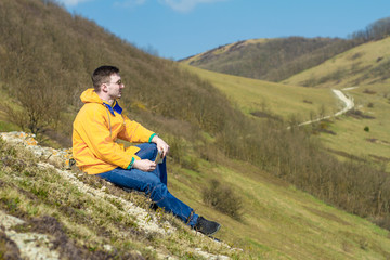 Naklejka na ściany i meble A tourist in a yellow jacket sits and looks at the mountains. Travel concept.
