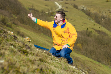 A tourist in a yellow jacket and glasses photographs himself on the phone. Create a selfie. In the background mountains. Tourism concept.