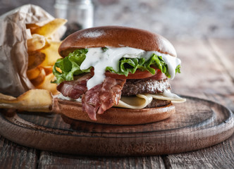  burger with bacon and cutlet with cheese, tomato, greens. served with fries and beer on a wooden table