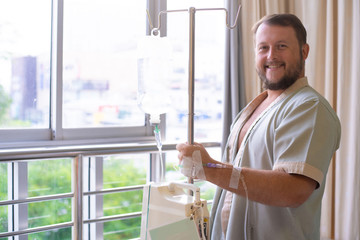 patient with a dropper looks out the window of the hospital room and smiles. Healthcare concept